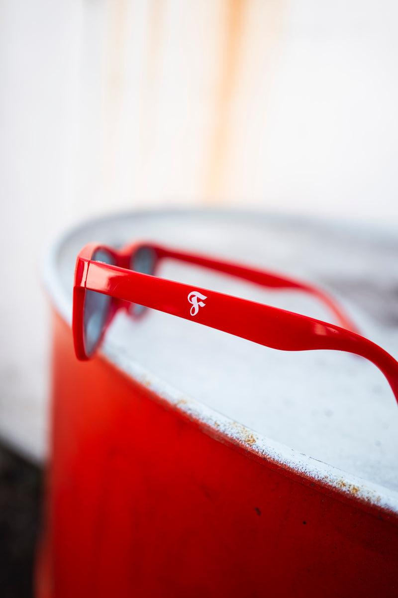 Nahaufnahme einer roten Sonnenbrille mit Fortuna-Logo auf dem
Bügel, platziert auf einem roten Metallfass.