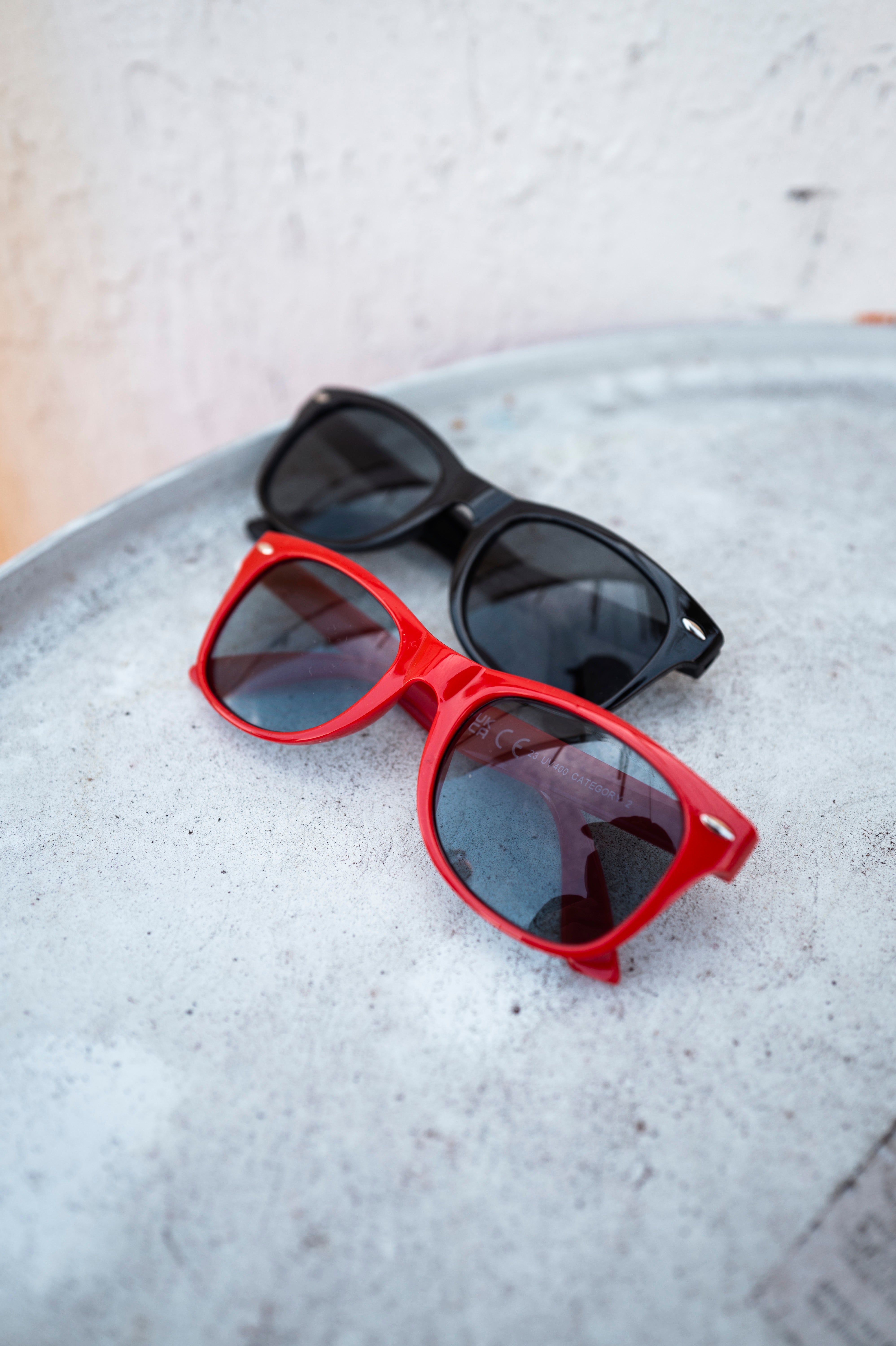 Schwarze und rote Sonnenbrille
mit Fortuna-Logo auf den Bügeln, liegend auf einer silbernen Metalloberfläche.
