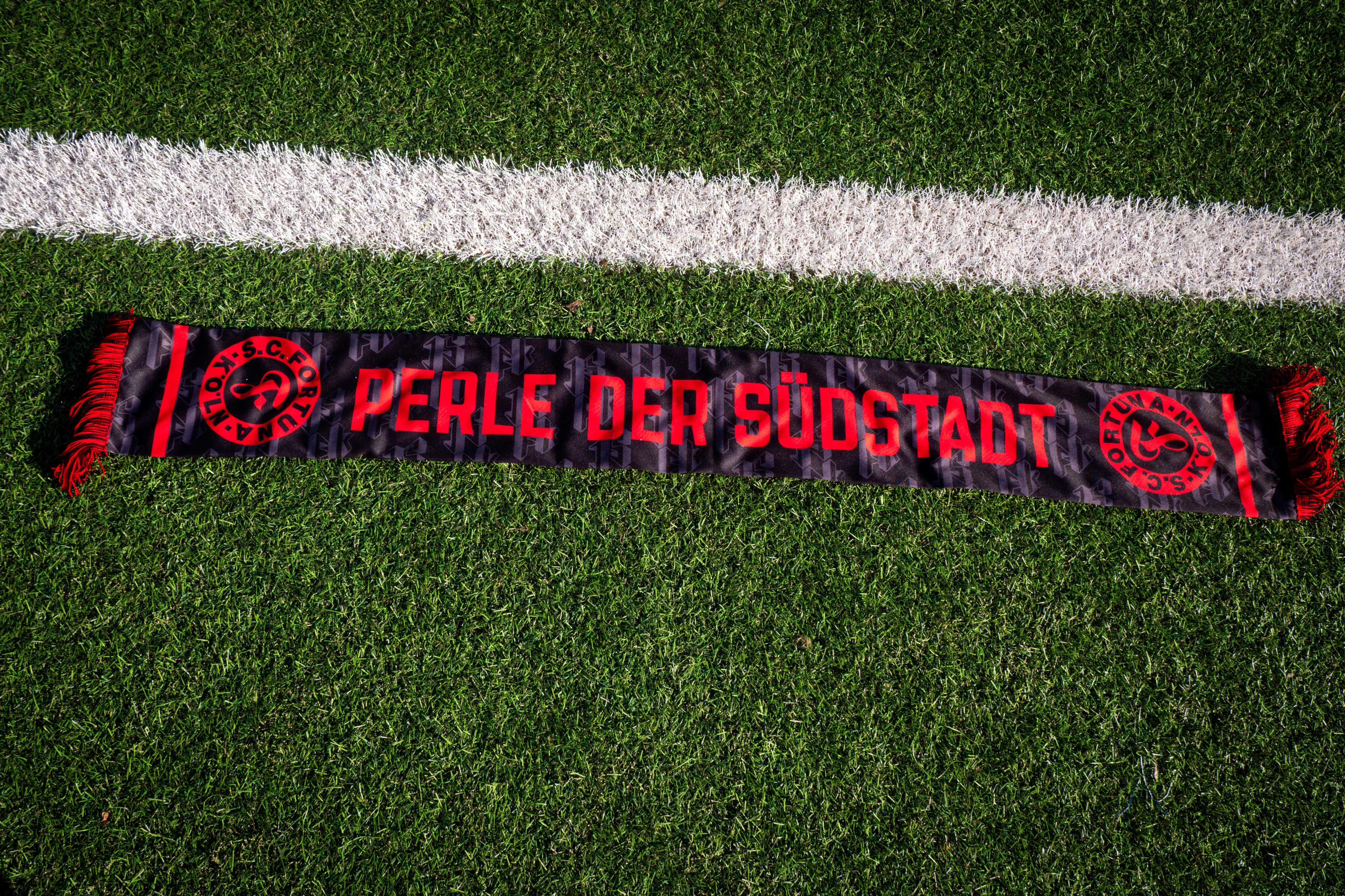schwarz-roter Schal liegt auf einem Fußballplatz.