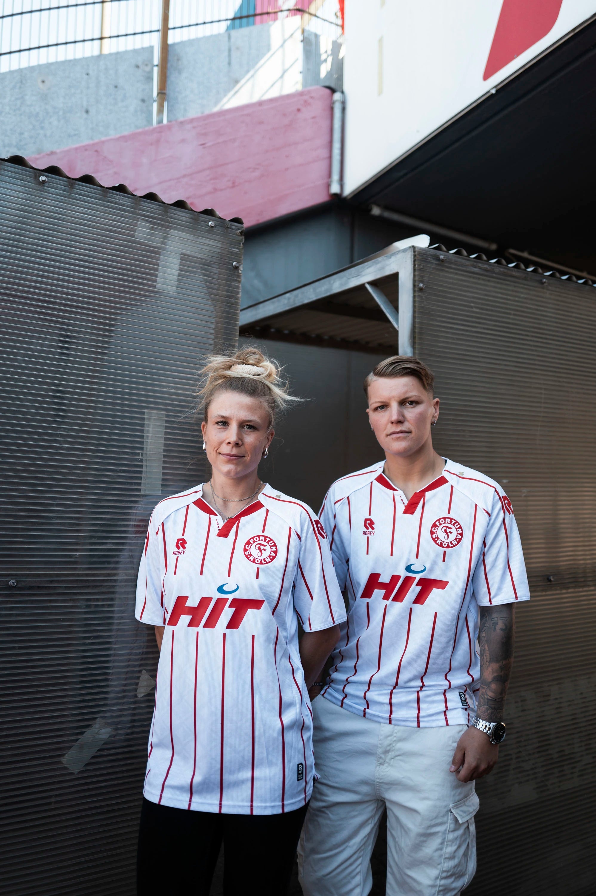 Zwei Spielerinnen tragen das neue
Heimtrikot der Saison 2025/2026.
Das Trikot ist weiß mit roten
Streifen. Auf der Brust befindet
sich das rot-weiße Fortuna-Logo
sowie ein rotes Robey-Logo, was
sich ebenfalls auf der Schulter
finden lässt. Zentral auf dem Trikot
befindet sich ein großes
Sponsoren-Logo von HIT.