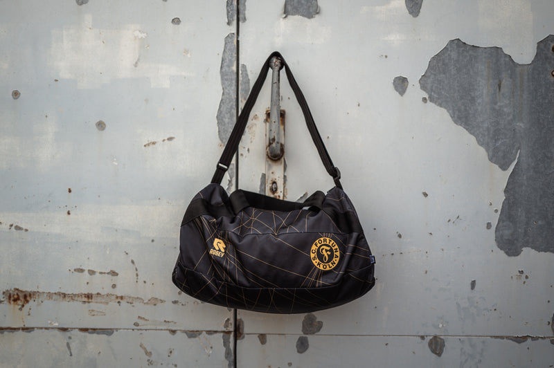 Auf diesem Bild sieht man die Schwarze Wochenender Tasche an einer Grauen Metalltür am Hacken hängen. 