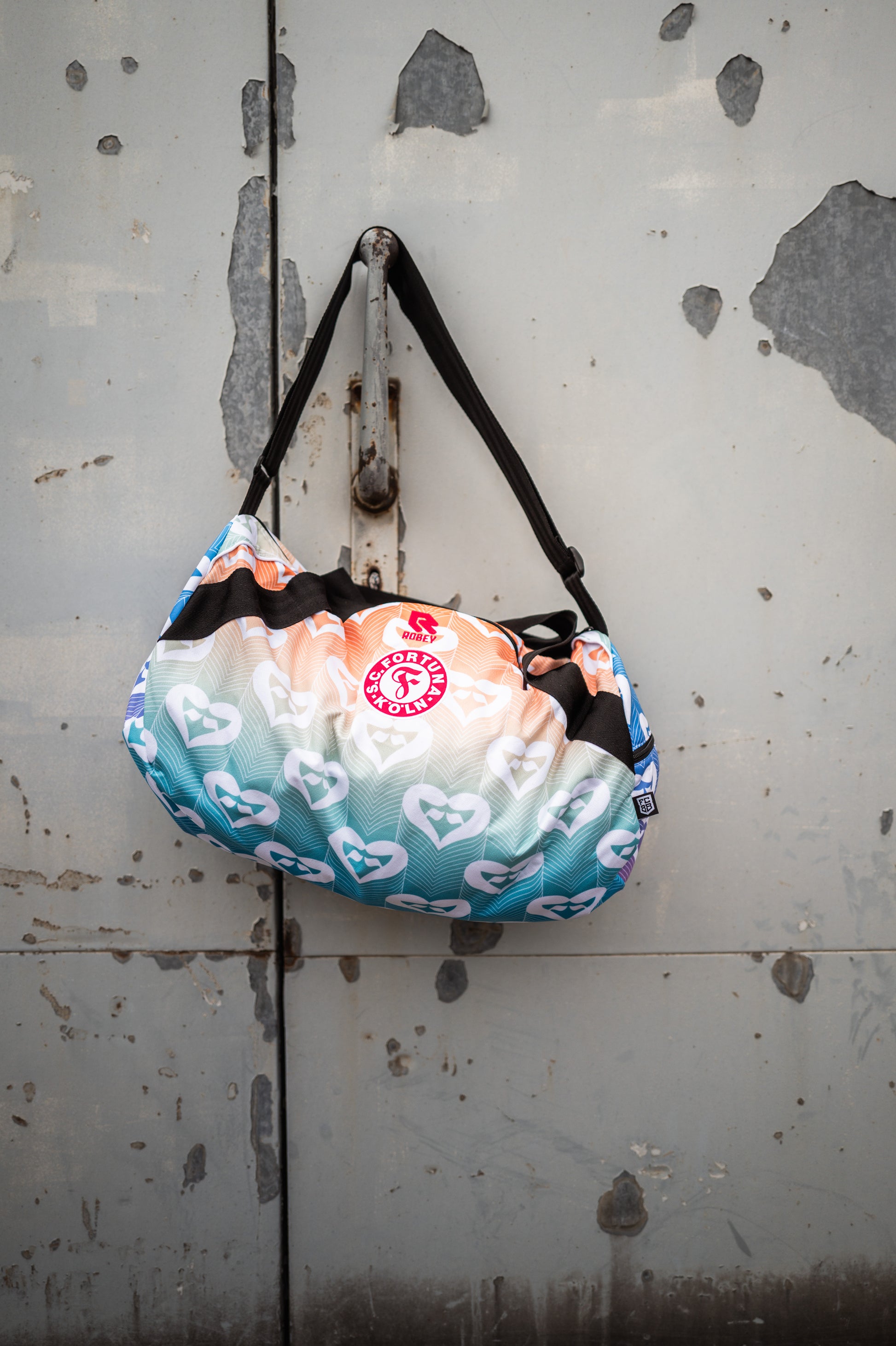 Auf dem Bild hängt die Pride Tasche einem Hacken an einer Grauen Metalltür.