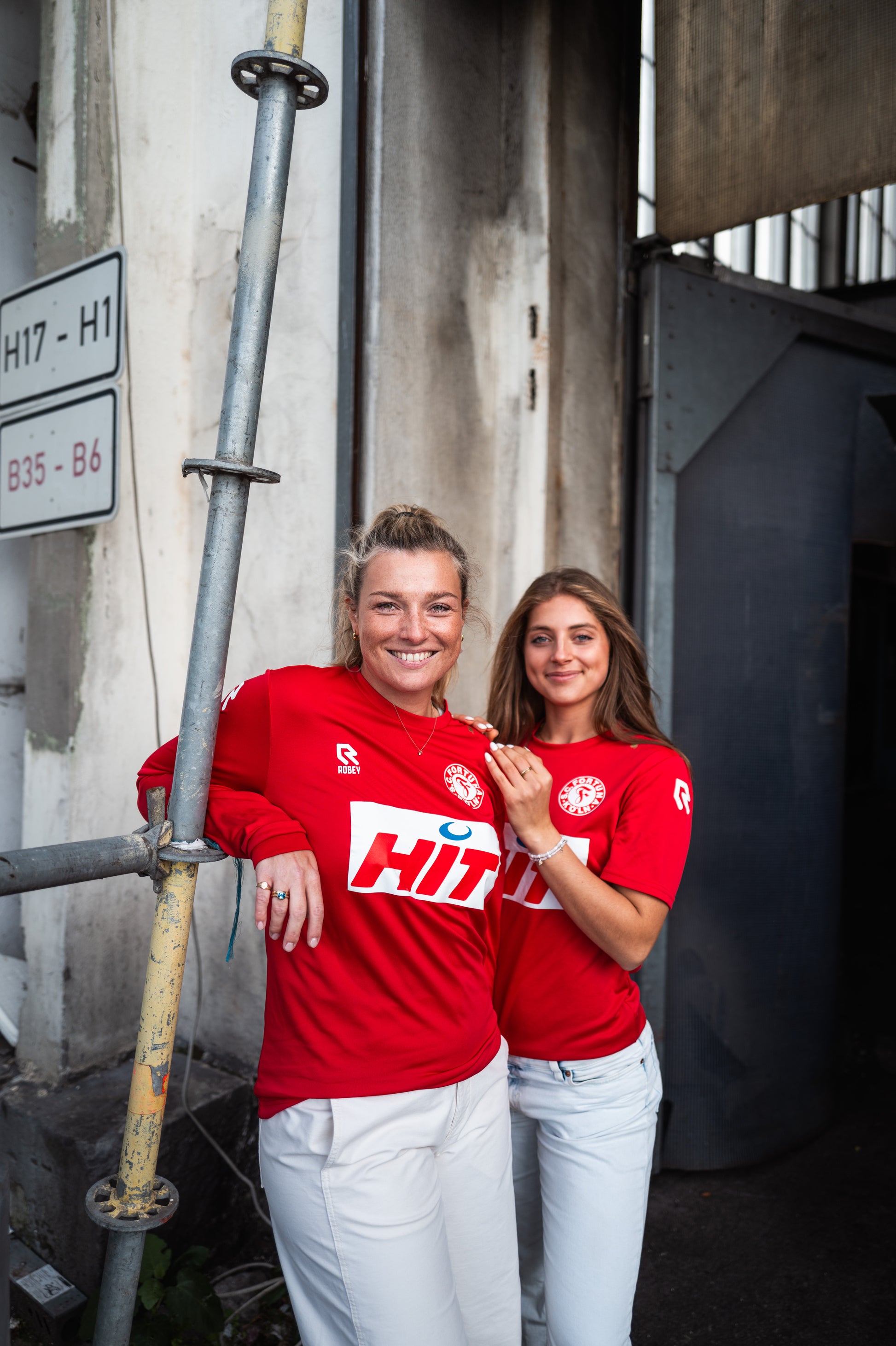 Die Dame links trägt das langarm-Trainingsshirt von Fortuna Köln. Rechts neben ihr trägt eine Dame das kurzarm-Trainingsshirt von Fortuna Köln.