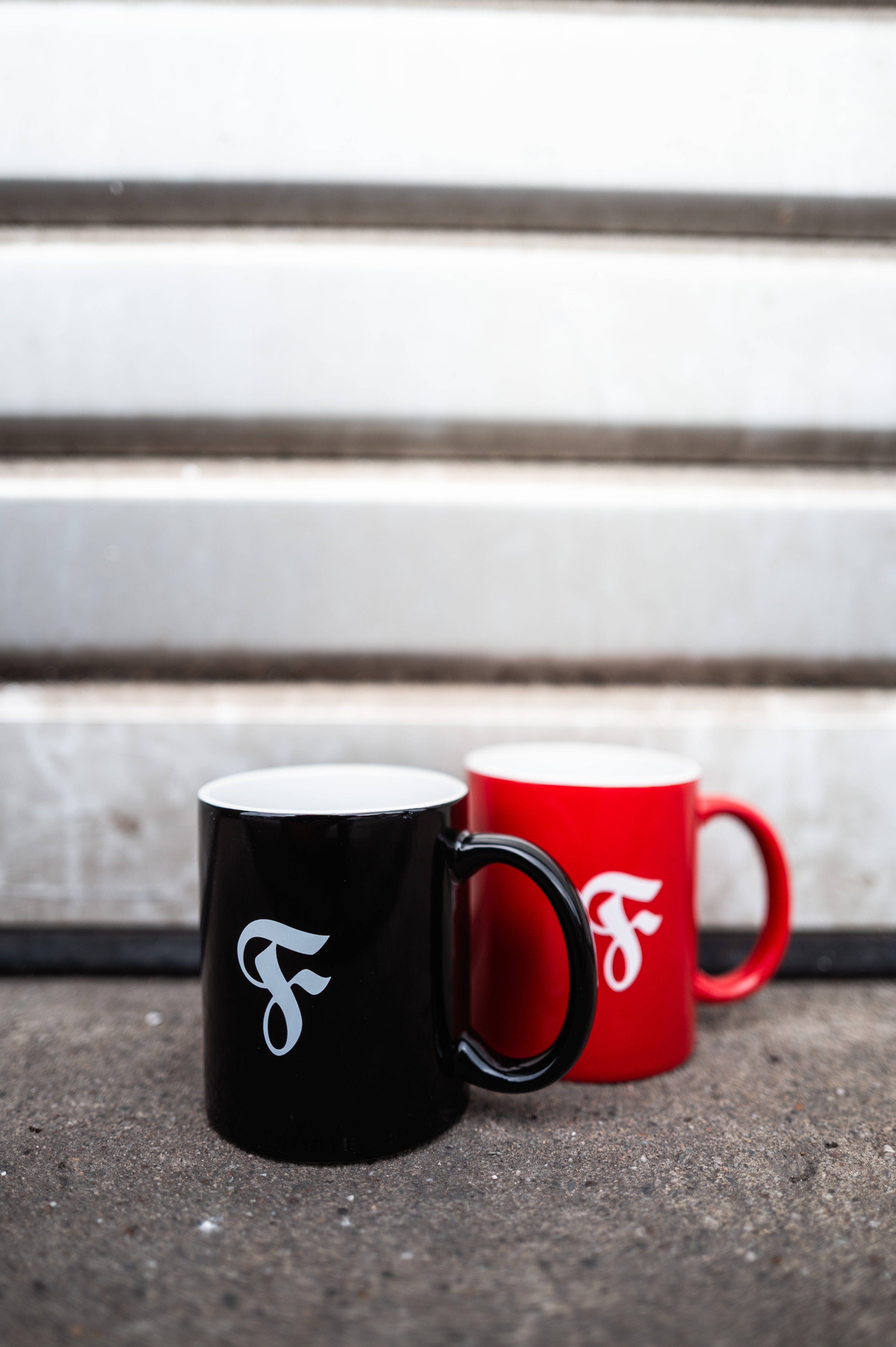 Rote & Schwarze Tasse stehen nebeneinander auf dem Boden.